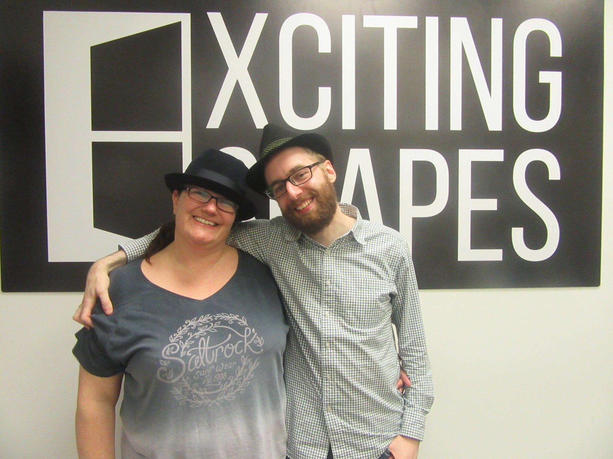 Anthony and Trenna pose after A Hidden Past at Exciting Escapes, beneath the Xciting Escapes wall sign.