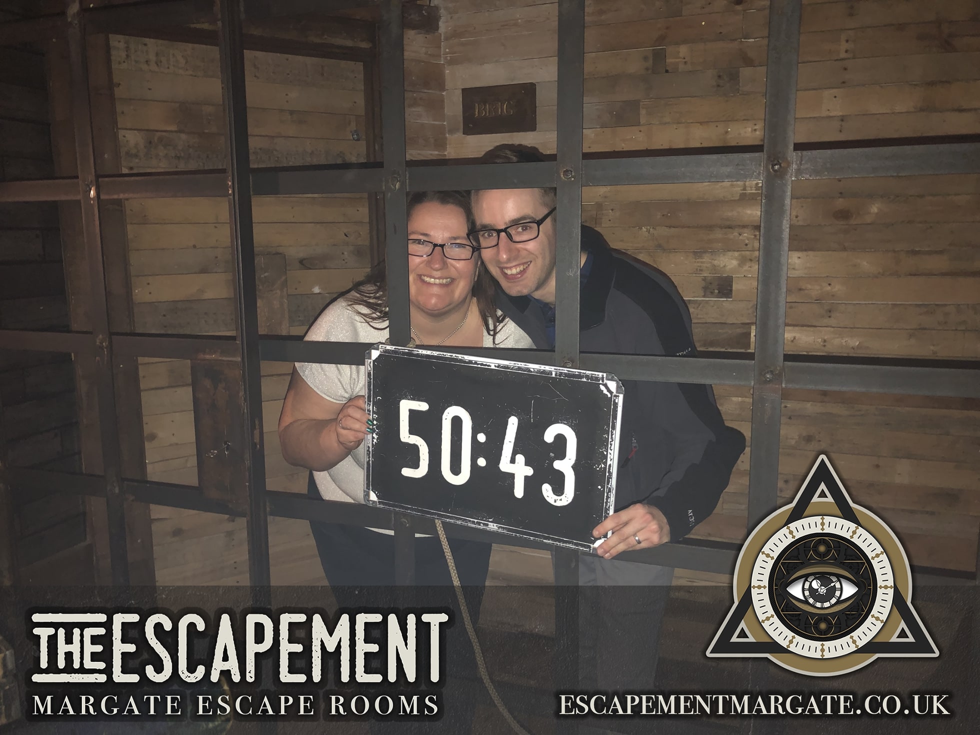 Anthony and Trenna pose after Pirates of Polaris at The Escapement, behind bars with a finish-time board.