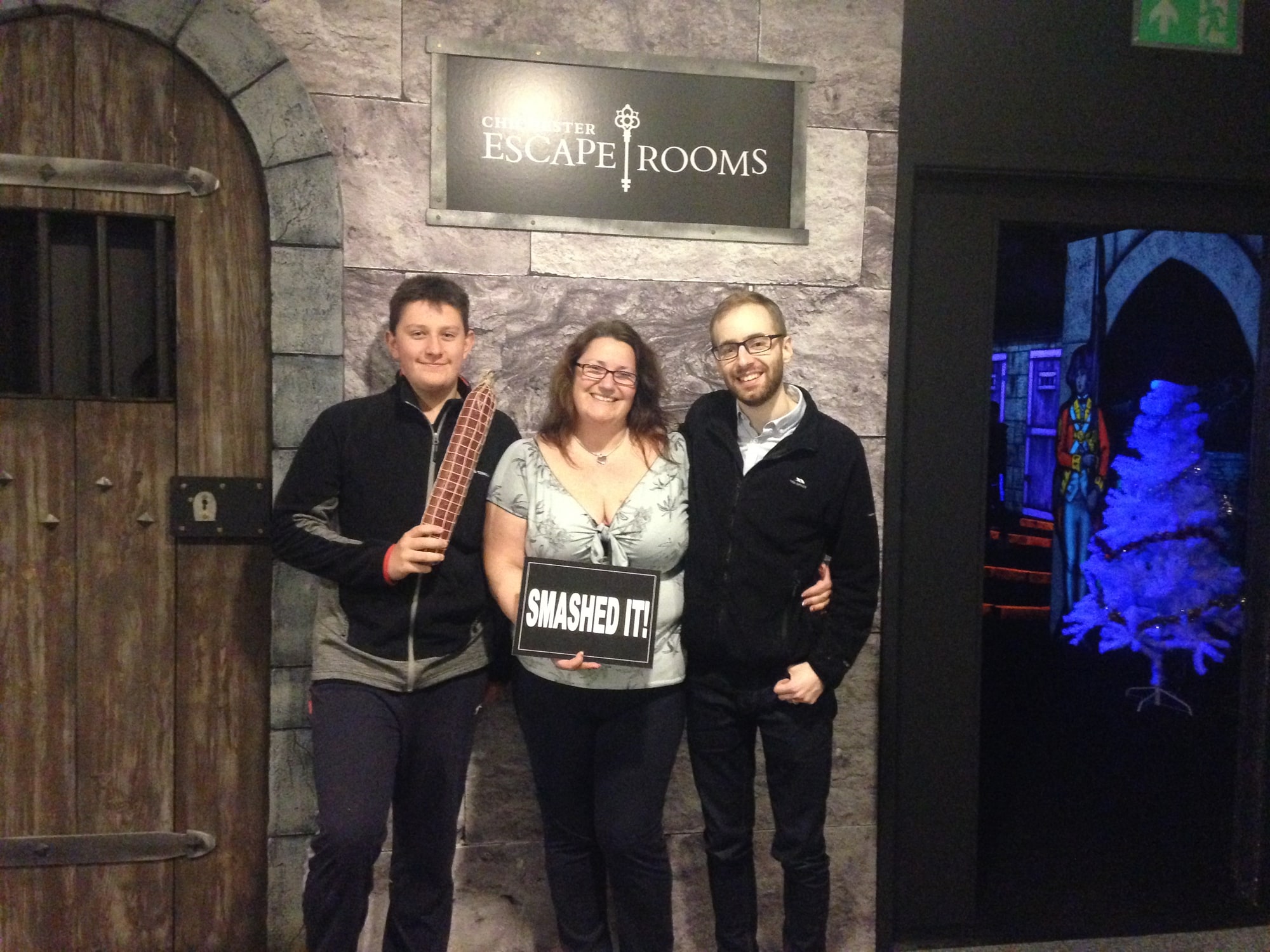 A three-person team pose after Cabin in the woods at Chichester Escape Room, in a castle-themed finish-photo setting.