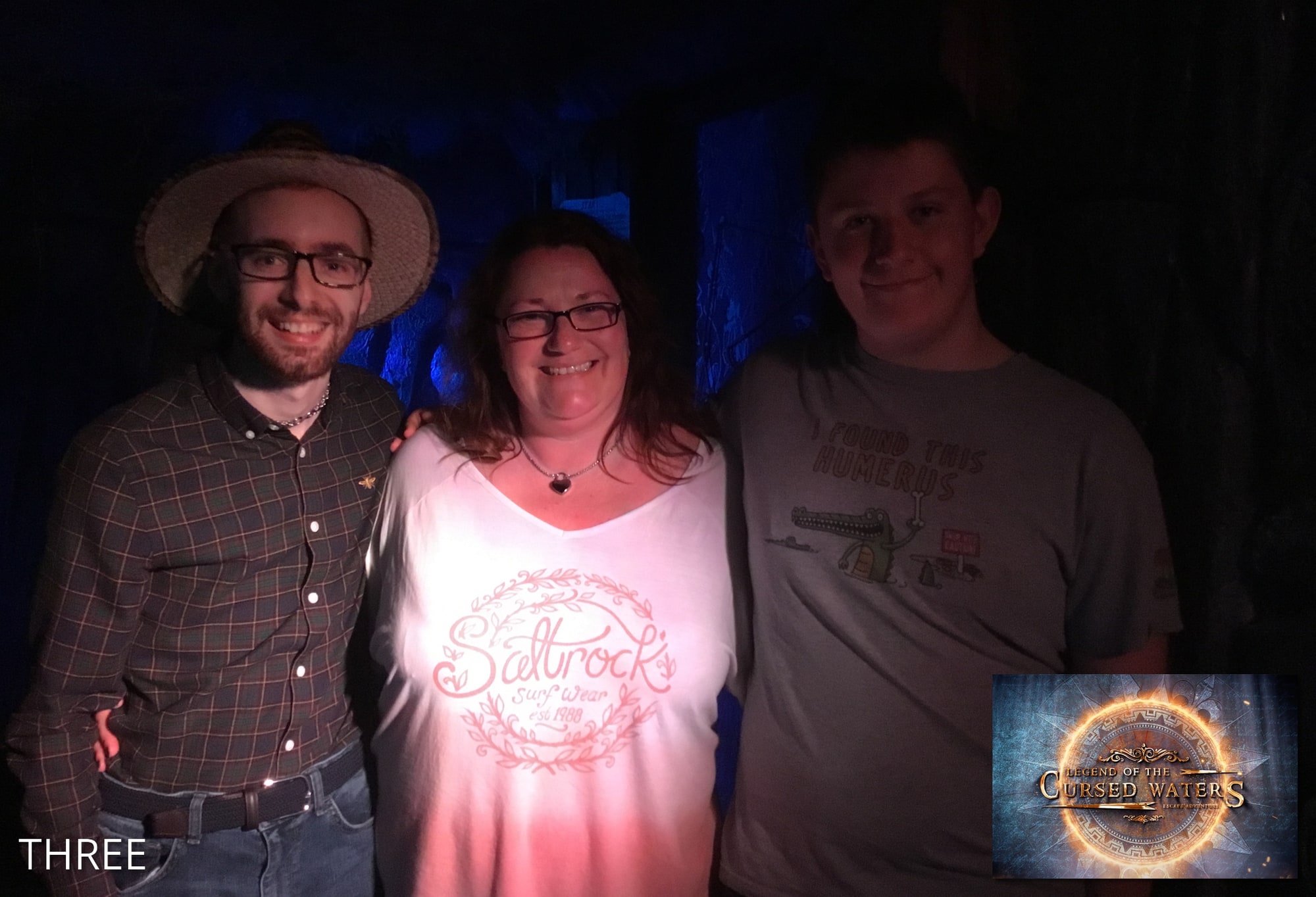 A three-person team pose after Cursed Waters at Ellusion, beneath Legend of the Cursed Waters branding.