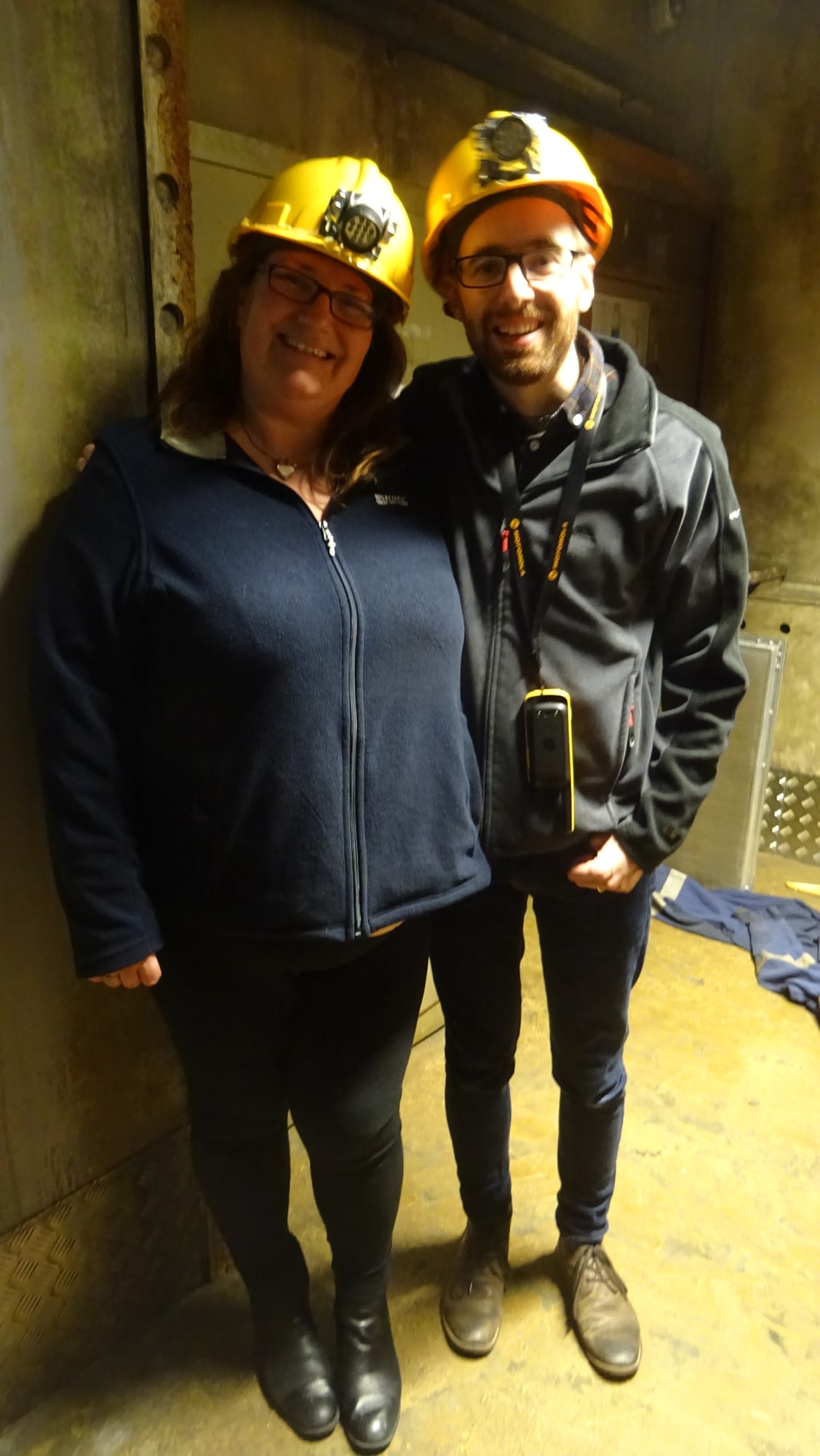 Anthony and Trenna pose after The Rig at letsxscape, wearing yellow hard hats in the industrial room.