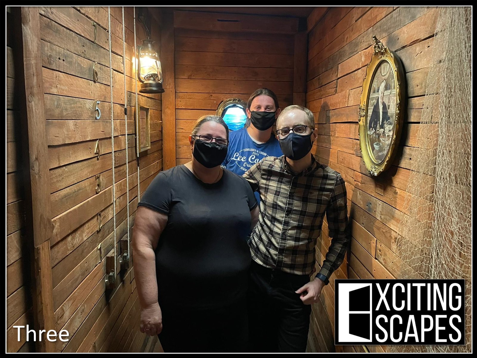 A three-person team pose after Disappearing Duchess at Exciting Escapes, in the narrow wooden room with lanterns.