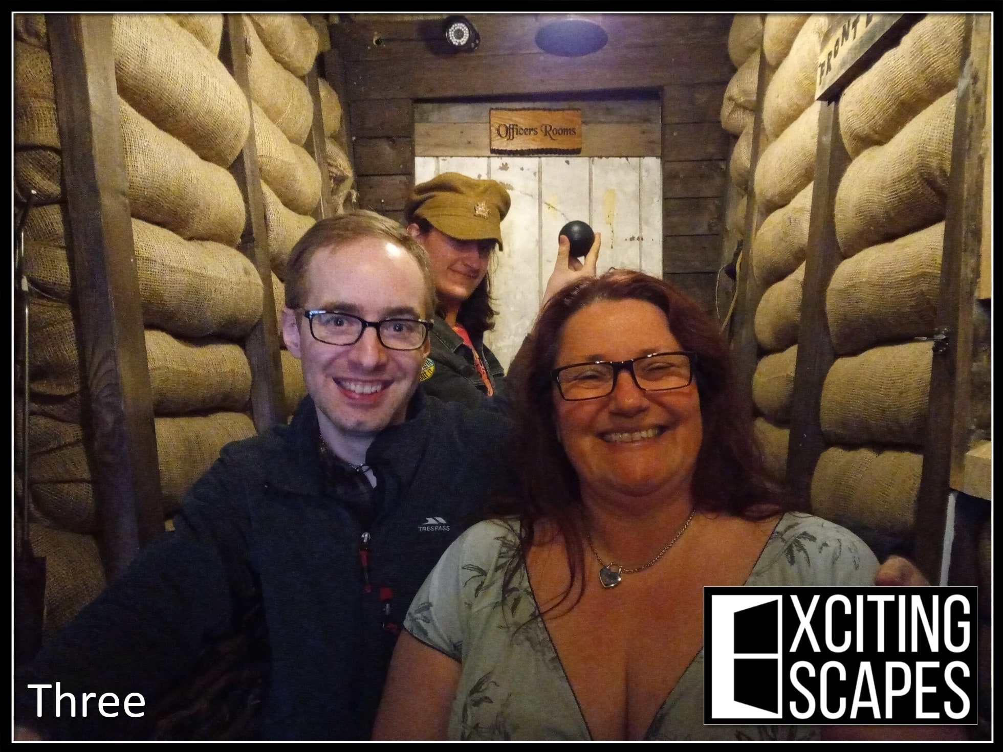 A three-person team pose after Disappearing Duchess part 2 at Exciting Escapes, in the sandbag-lined military corridor.