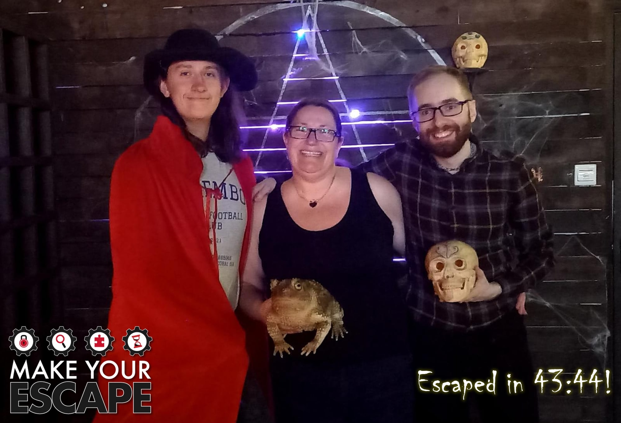A three-person team pose after Spellbound at Make your escape, in the cobwebbed spooky room with skull props.