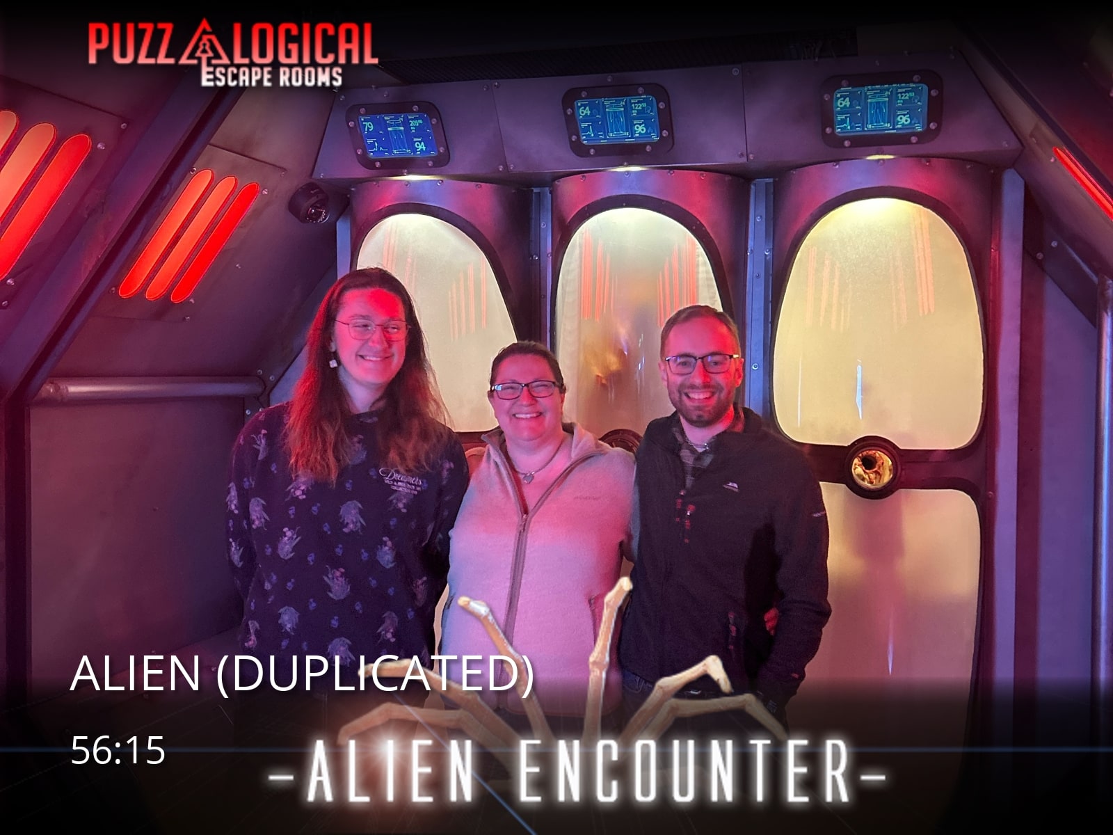 A three-person team pose after Alien at Puzzelogical, in the red-lit spaceship room.