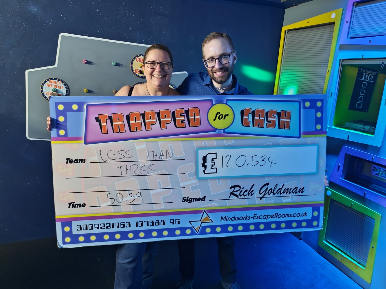 Anthony and Trenna pose after Trapped for Cash at Mindworks, holding the Trapped for Cash cheque prop.