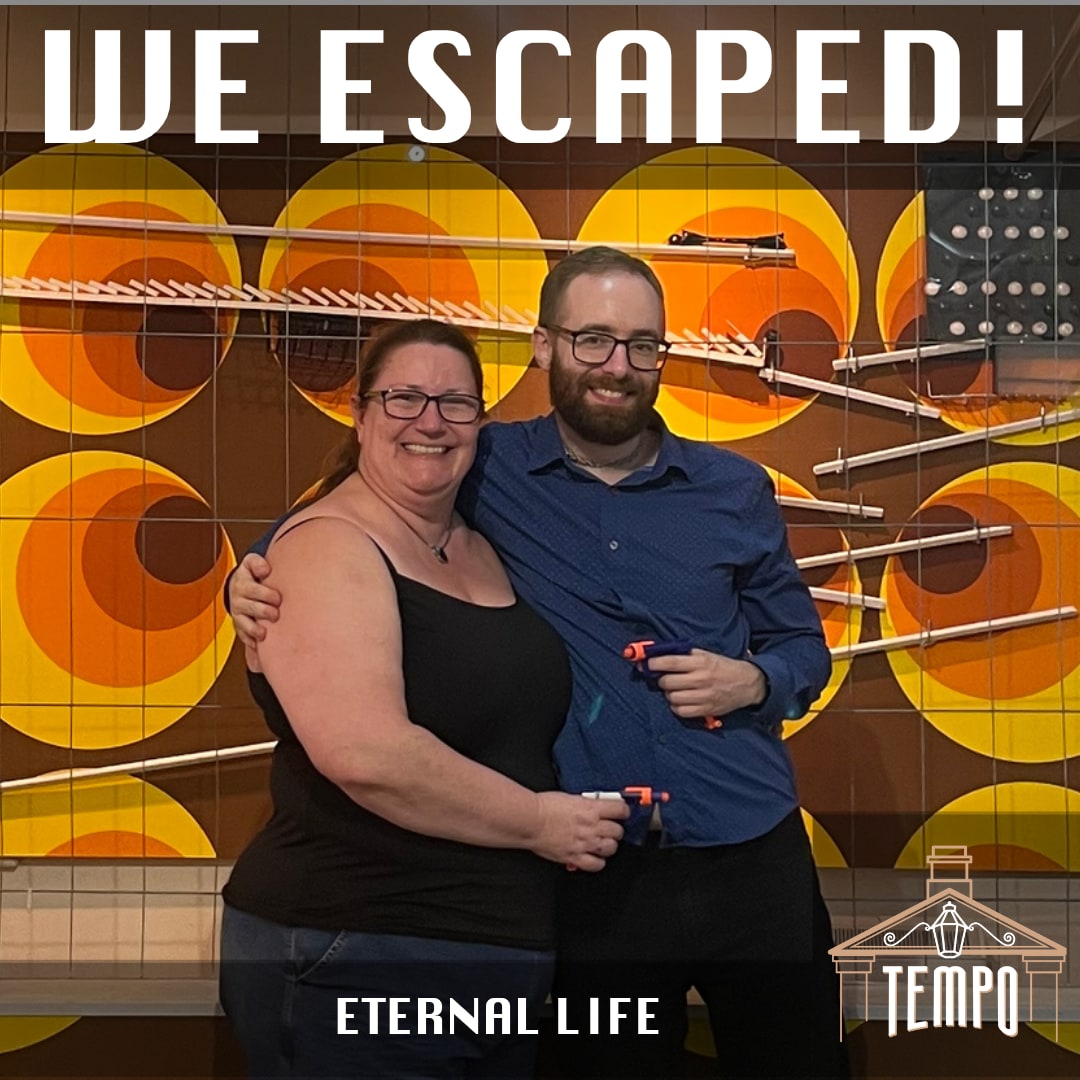 Anthony and Trenna pose after Eternal Life at Tempo Escape Room Bath, before the retro Eternal Life finish-photo backdrop.