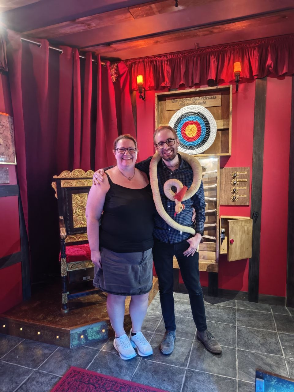 Anthony and Trenna smiling after completing Robin Hood at Break Escape, with Anthony wearing a large toy snake in front of an archery target.